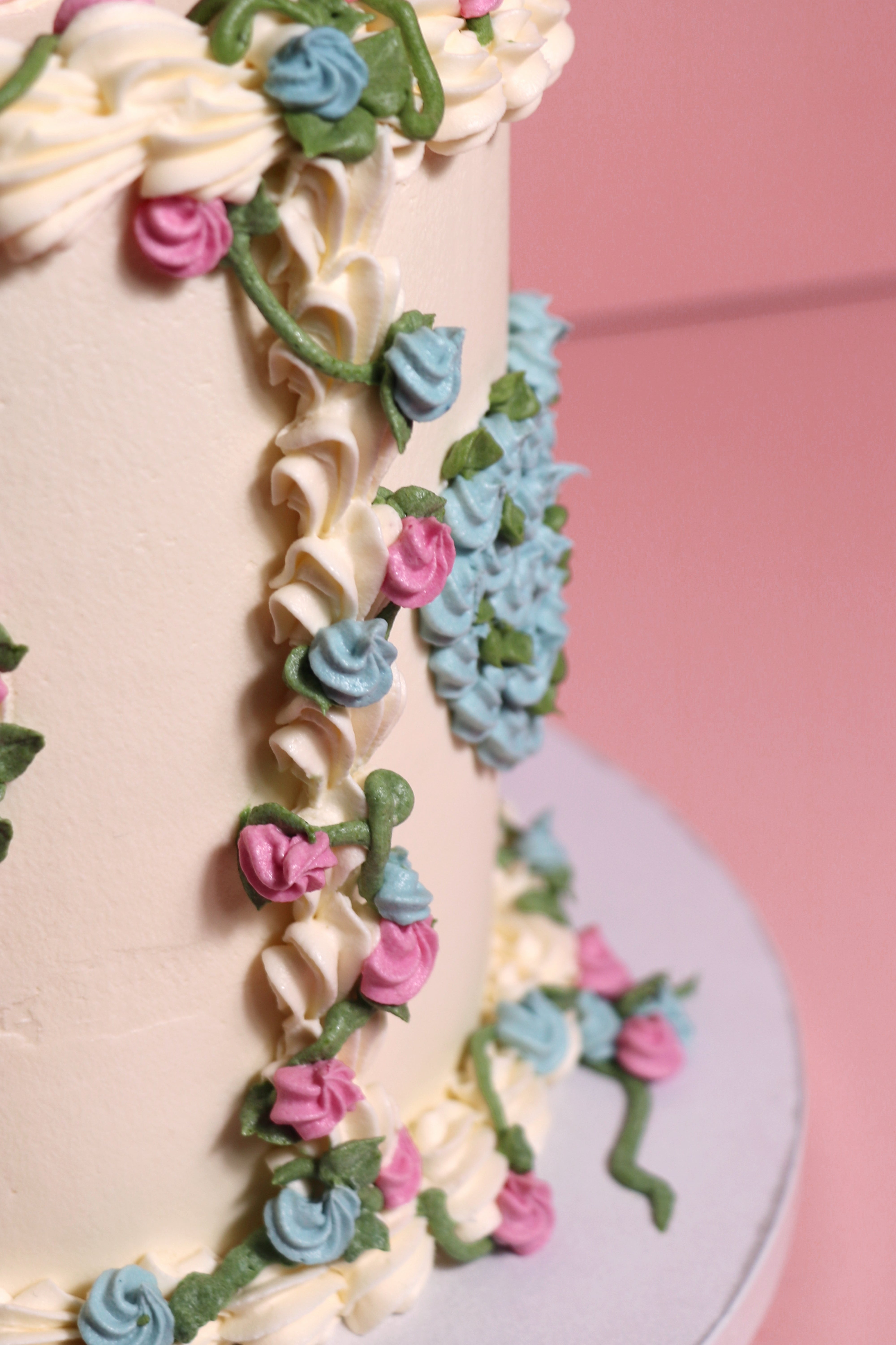 Gender reveal floral and vines cake with pink and blue piping with a heart shaped mortif handmade by Cakasion in Uxbridge.