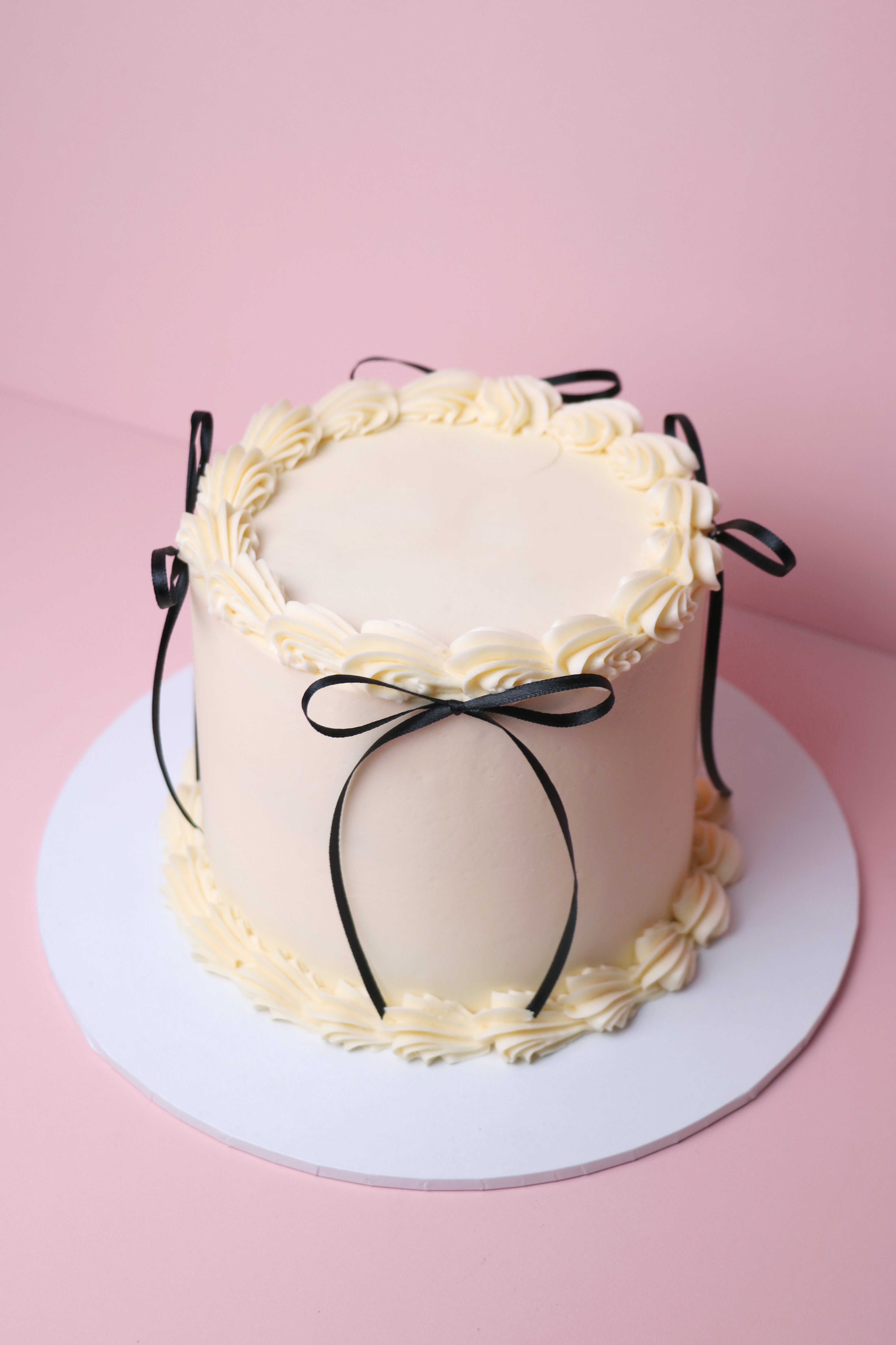 Minimalist white buttercream cake with piped swirls and black satin bows, handmade in Uxbridge by CakeasionShop