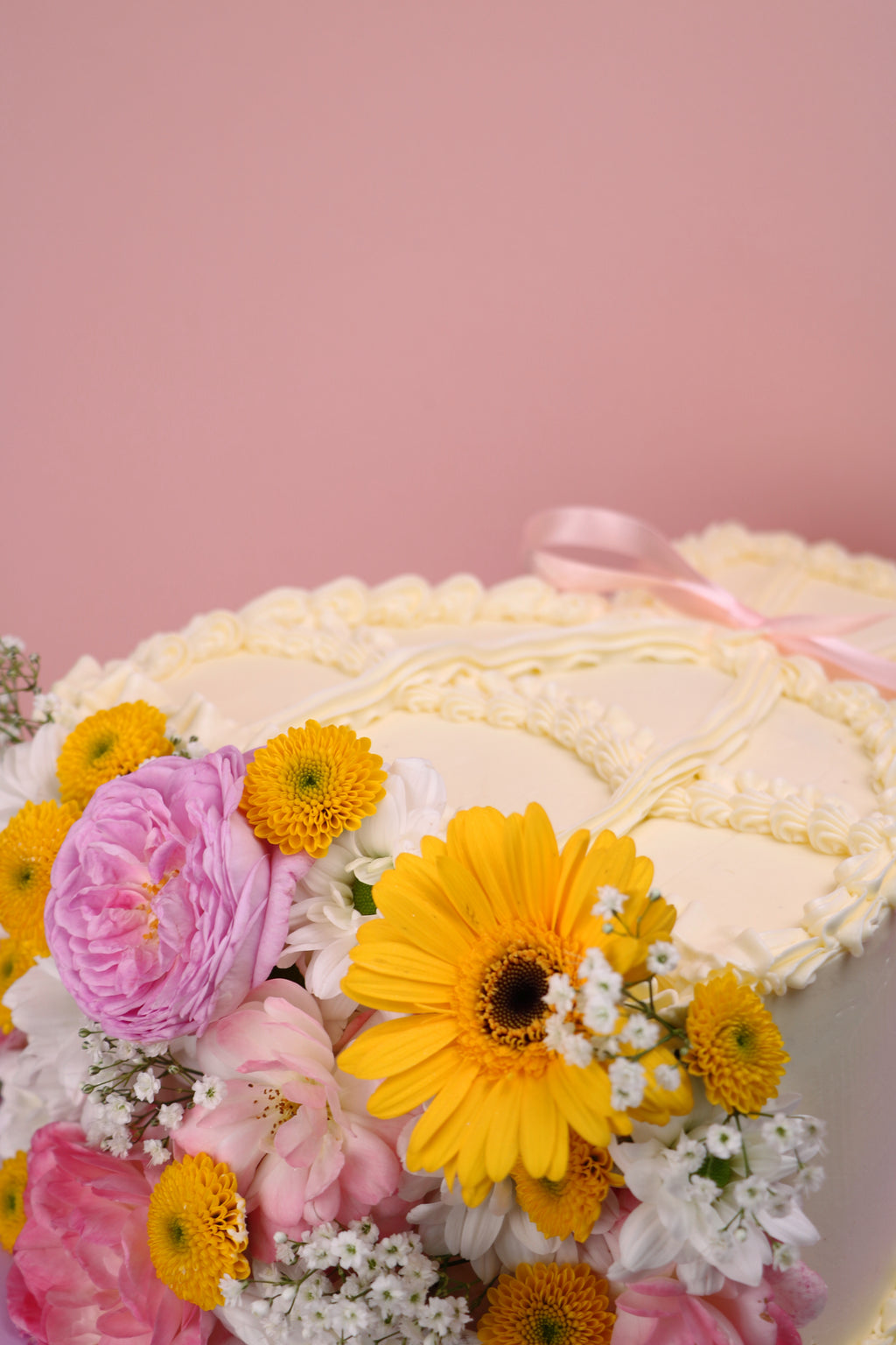 Heart-shaped fresh flower cake with yellow daisies, pink roses and vintage piped buttercream on lilac board handmade by Cakeasion in Uxbridge.