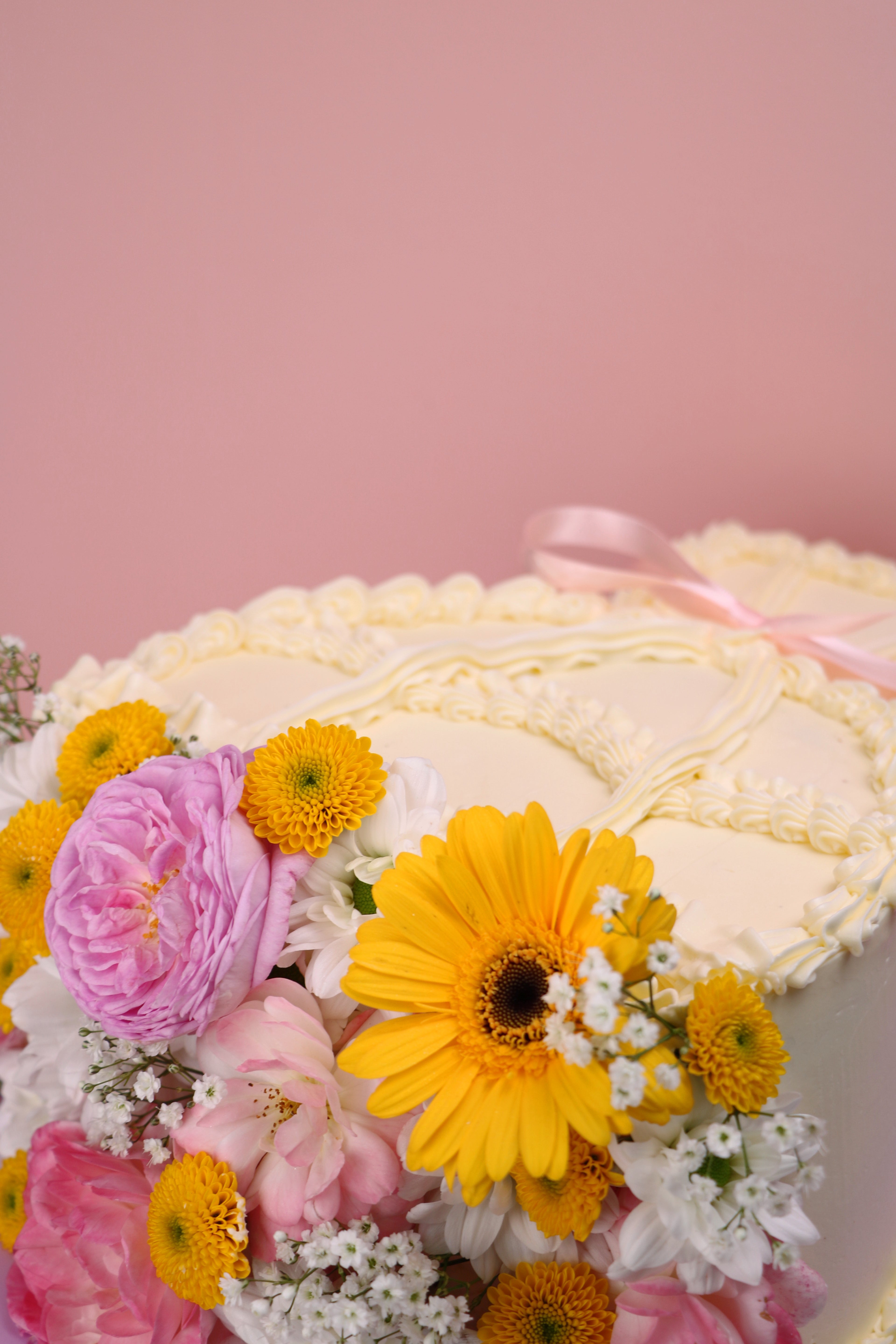 Heart-shaped fresh flower cake with yellow daisies, pink roses and vintage piped buttercream on lilac board handmade by Cakeasion in Uxbridge.