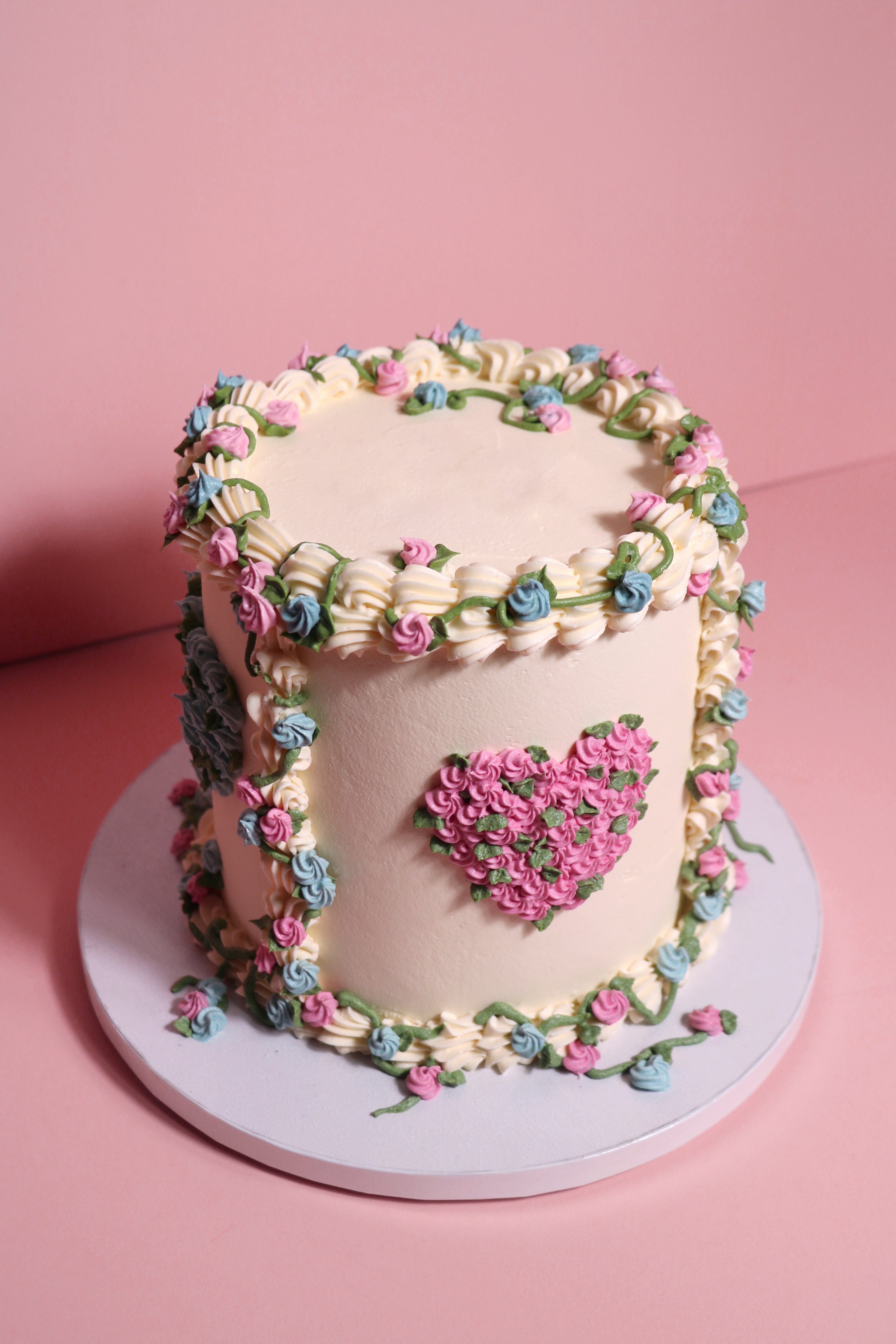 Gender reveal floral and vines cake with pink and blue piping with a heart shaped mortif handmade by Cakasion in Uxbridge.