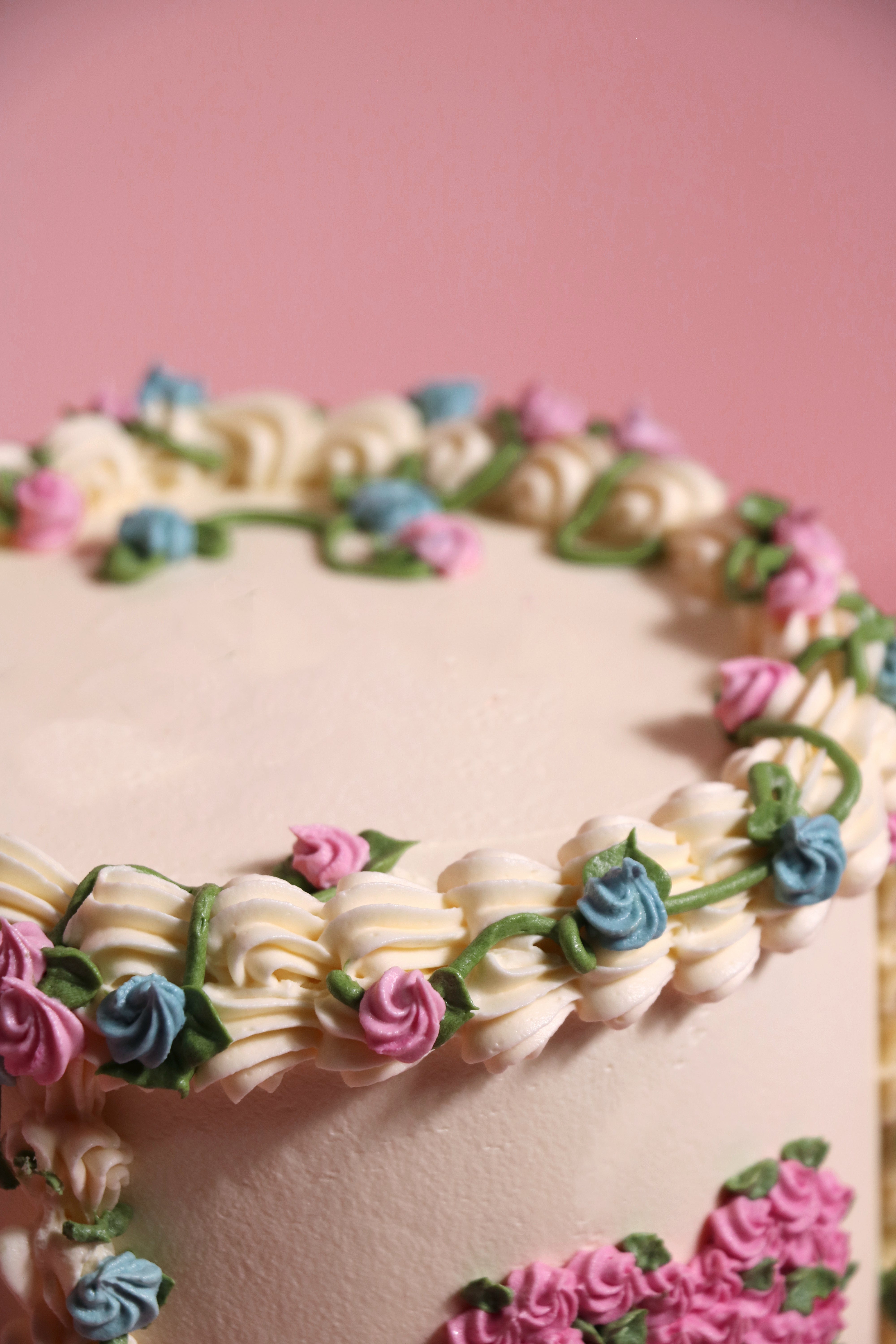 Close up of a Gender reveal floral and vines cake with pink and blue piping with a heart shaped mortif handmade by Cakasion in Uxbridge.
