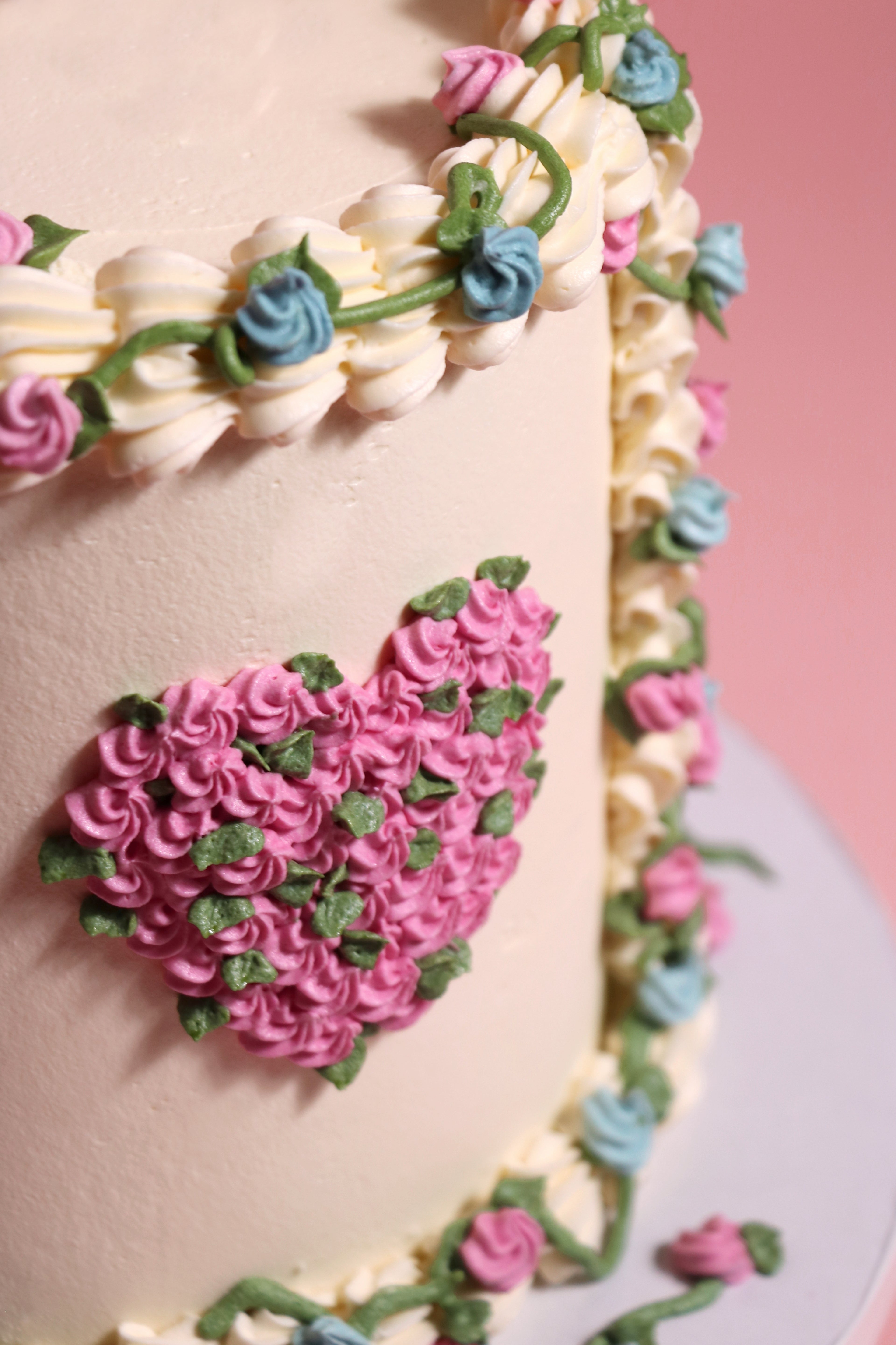 Decorative cake with pink heart, flowers, and green leaves on a pink background