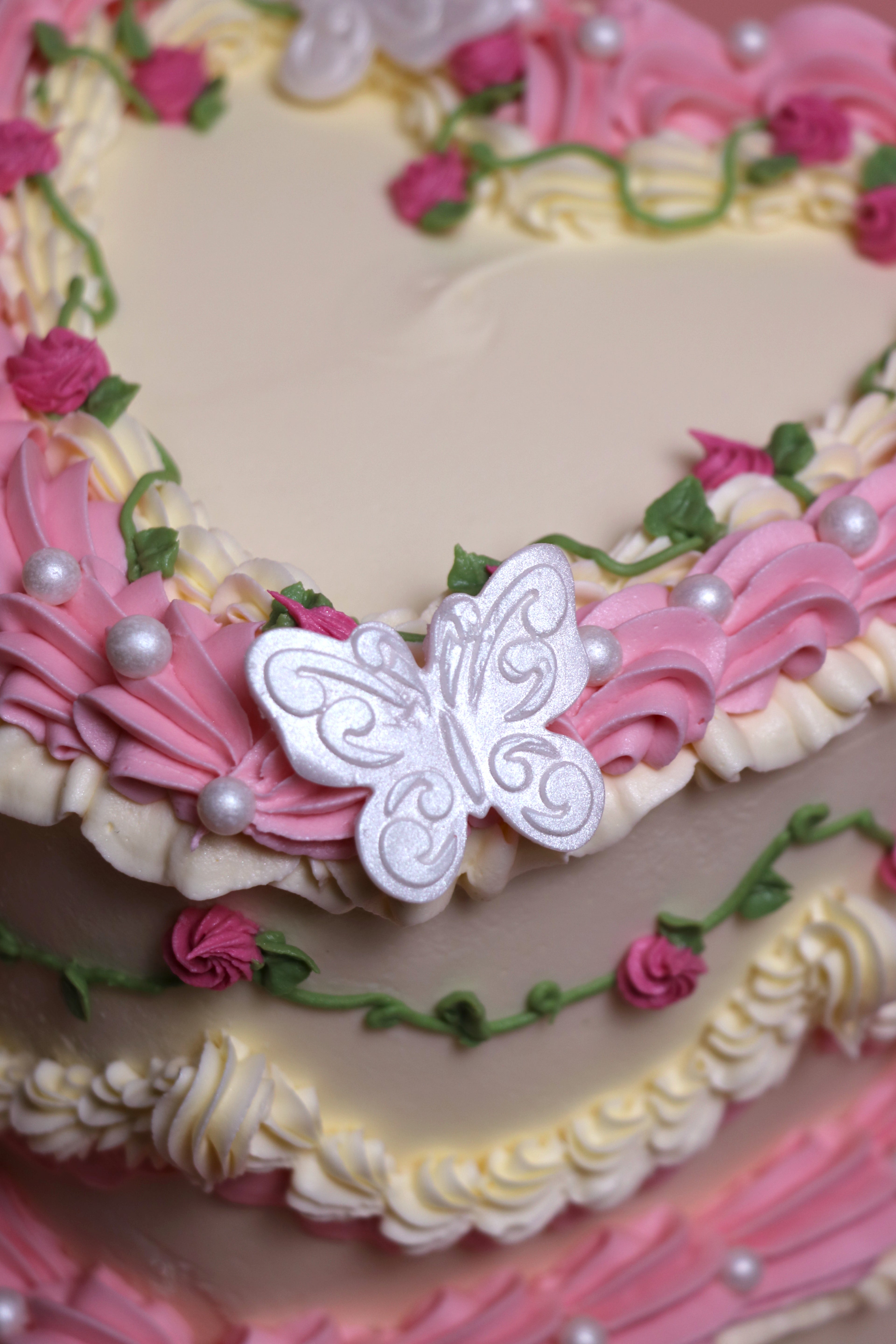 Close up of a Heart-shaped vintage-style birthday cake with piped pink roses and faux pearl details from Cakeasion Shop Uxbridge.