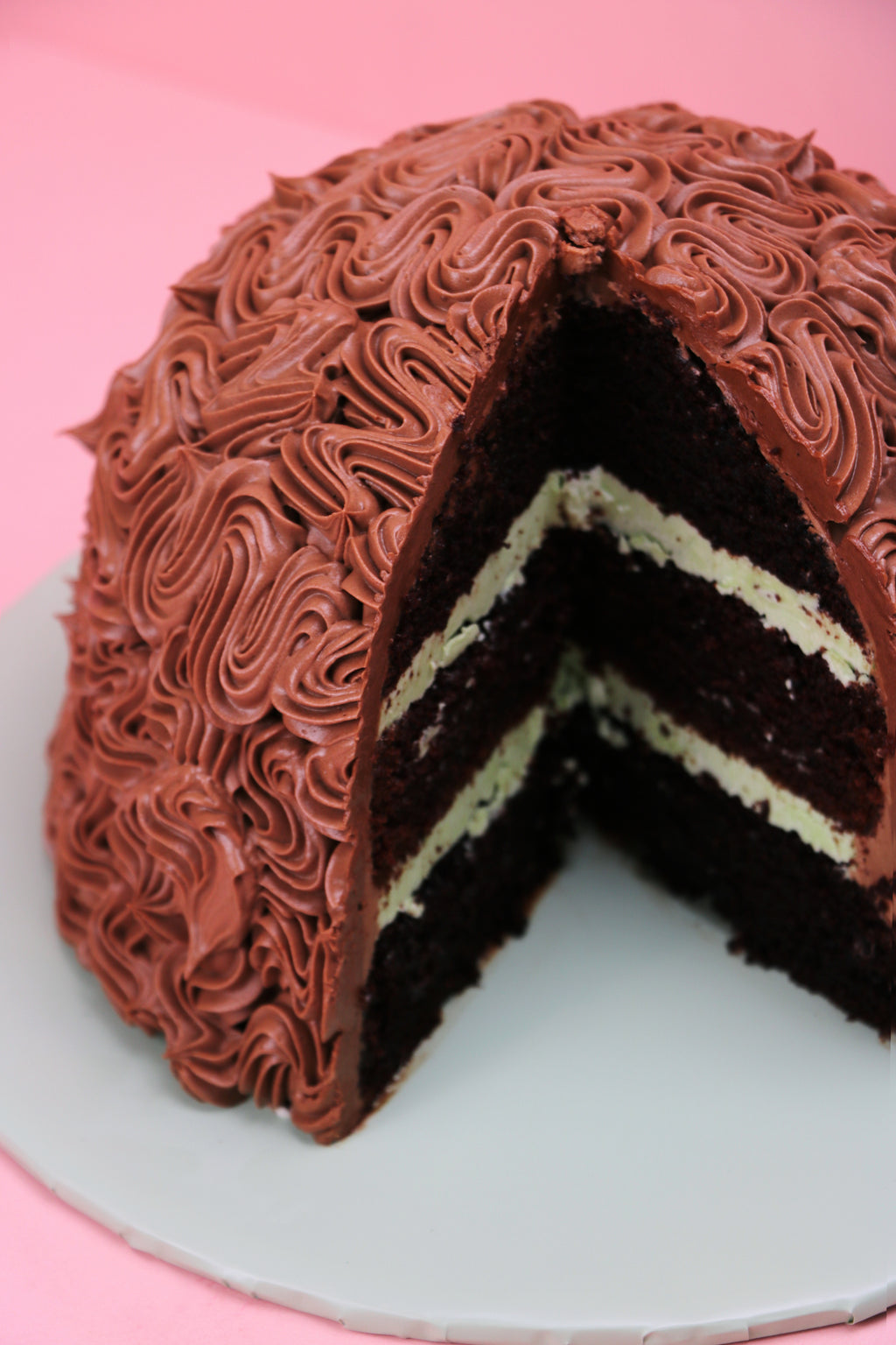 Slice cut out of a mint chocolate dome cake with piped chocolate buttercream design, Swirl piped chocolate dome cake with mint buttercream filling, Dome-shaped chocolate cake with rich buttercream texture made by Cakeasion in Uxbridge.