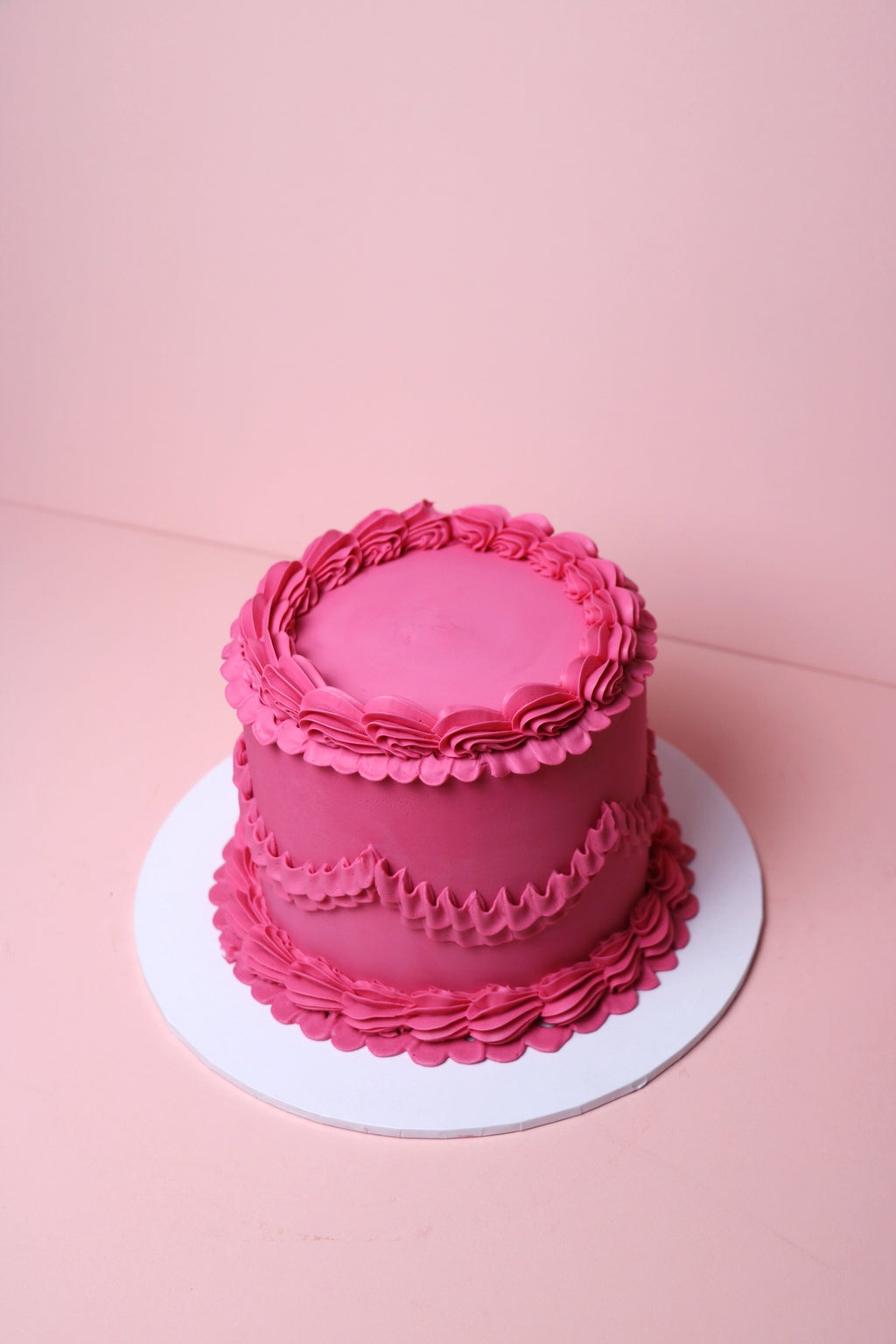 Pink cake with ruffled frosting on a pink background from Cakeasion Shop -serving Uxbridge, Hayes, and surrounding west london areas