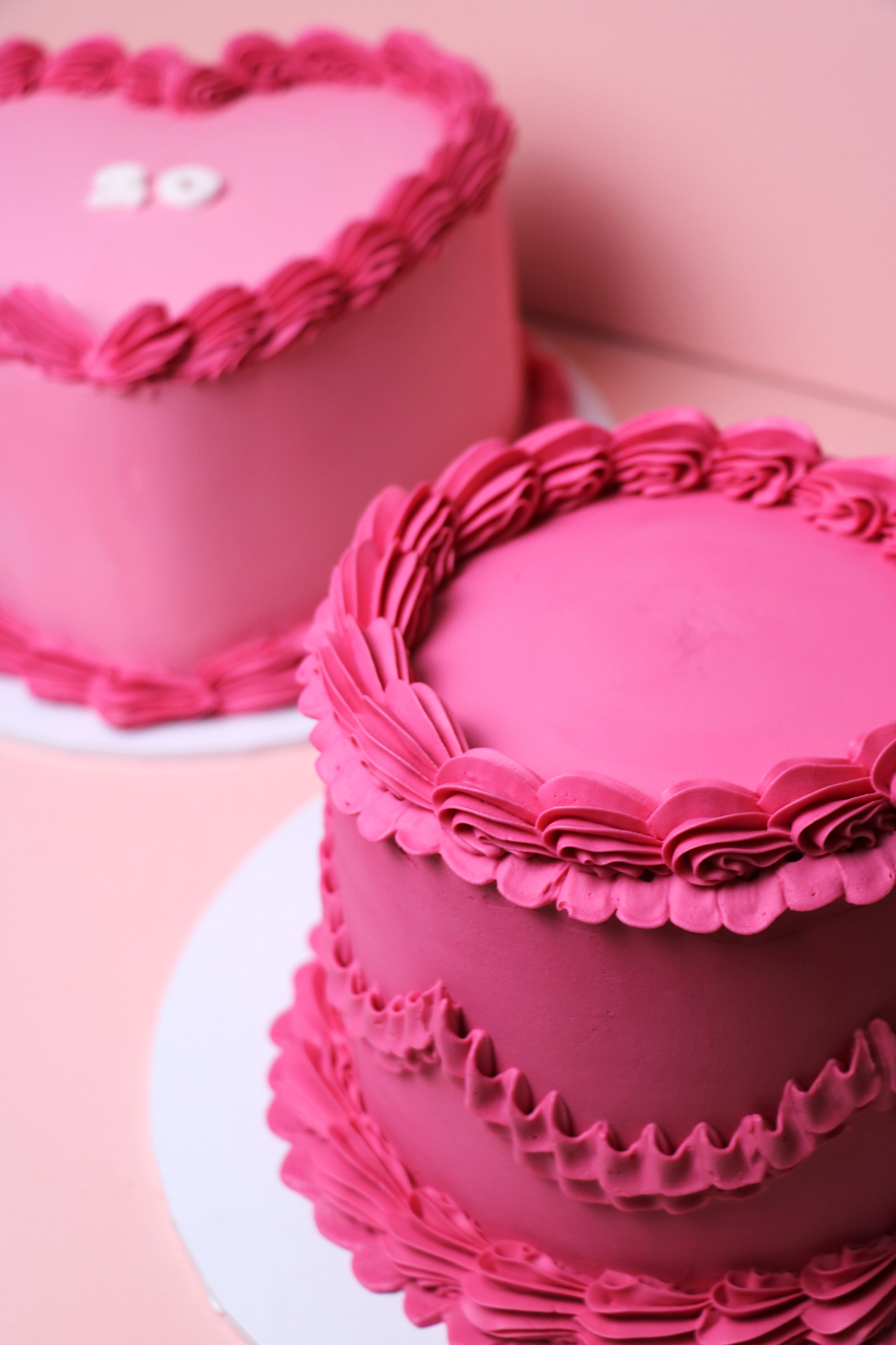Round and heart pink minimalist cakes with decorative frosting on a light pink background from Cakeasion Shop - serving Uxbridge, Hayes, and surrounding west london areas