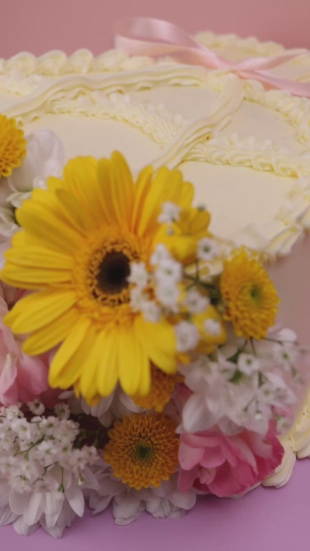 Video of a Heart-shaped fresh flower cake with yellow daisies, pink roses and vintage piped buttercream on lilac board handmade by Cakeasion in Uxbridge.